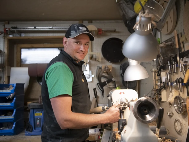 Da Doni Holzstiftmanufaktur Handwerker in einer Werkstatt bearbeitet Holz an einer Drehbank, umgeben von Werkzeugen.
