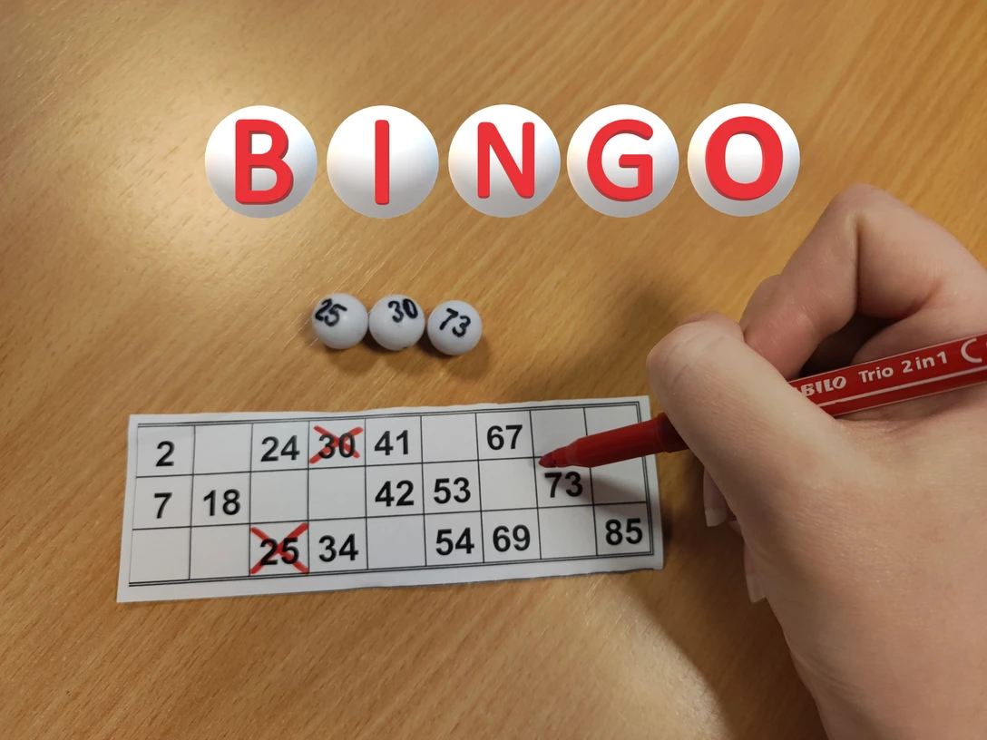 Bingo Hand markiert Zahlen auf einer Bingo-Karte; drei Kugeln mit 25, 30 und 73 vor rotem Stift.
