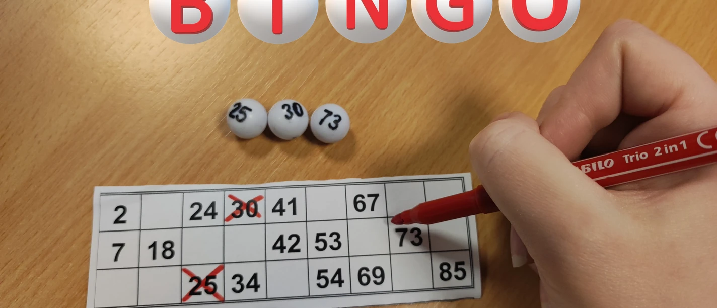 Bingo Hand markiert Zahlen auf einer Bingo-Karte; drei Kugeln mit 25, 30 und 73 vor rotem Stift.