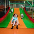 Rutsche im Solivital Sebnitz Vier Kinder rutschen lachend eine große, bunte Rutsche in einem Indoor-Spielplatz hinunter. Die Farben der Rutsche sind grün und orange.