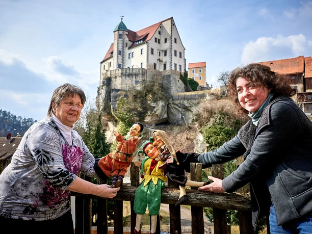 Kasperpuppen vor der Burg Hohnstein Zwei Frauen halten Handpuppen vor einer Burg auf einem Felsen; die Stimmung ist fröhlich und entspannt.