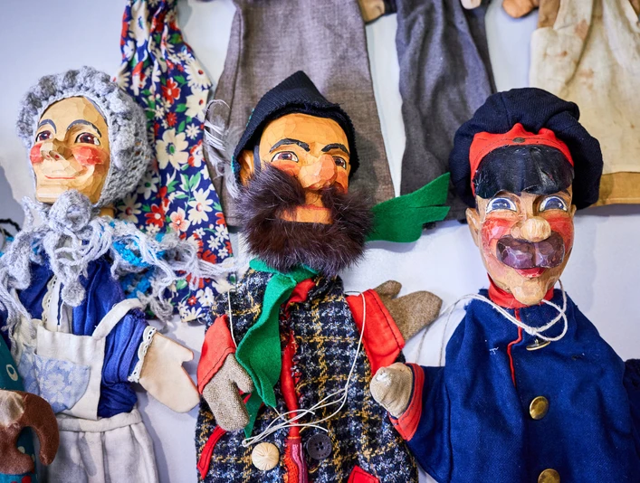 Kasperpuppen vom Max Jacob Theater Drei bunte Handpuppen mit fröhlichen Gesichtern, in traditionellen Kostümen, auf einem Tisch liegend.