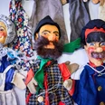 Poppen van het Max Jacob Theater Drei bunte Handpuppen mit fröhlichen Gesichtern, in traditionellen Kostümen, auf einem Tisch liegend.