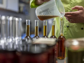 Mary's Marmeladen Flüssigkeit wird aus einem Messbecher in schlanke Glasflaschen gefüllt.