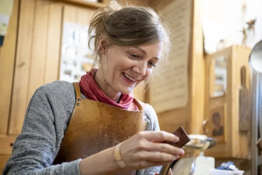 Holzdesign & Holzobjekte Eva Engler Inser Hoamat Partner Eine Frau arbeitet in einer Holzwerkstatt, trägt eine Lederschürze und schaut auf ein Werkstück.