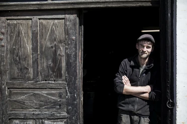 Aberl Metallgestaltung Ein Mann lehnt lächelnd in einer Balkontür eines alten Holzgebäudes.