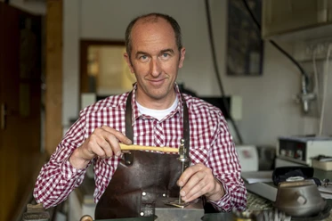 Der Graveur Kaufmann Graveur bei der Arbeit mit Werkzeug in einer Werkstatt, lächelnd in die Kamera blickend.