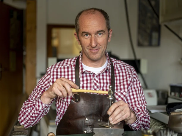 Der Graveur Kaufmann Graveur bei der Arbeit mit Werkzeug in einer Werkstatt, lächelnd in die Kamera blickend.
