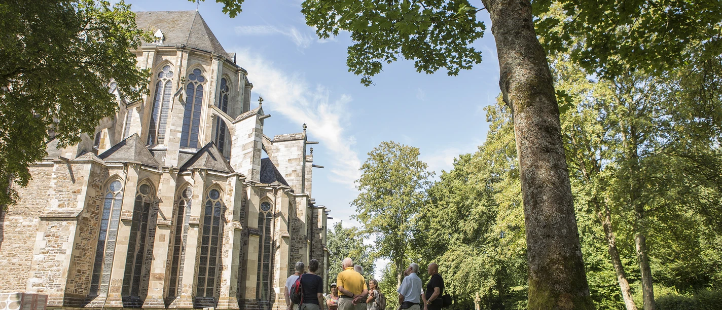 Führung in Altenberg Eine Gruppe steht vor der beeindruckenden Altenberger Domkirche umgeben von Bäumen und grünem Rasen.