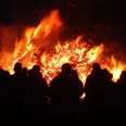 Feuer Personen stehen vor einem großen, lodernden Feuer in der Dunkelheit, die Flammen erhellen die Nacht.