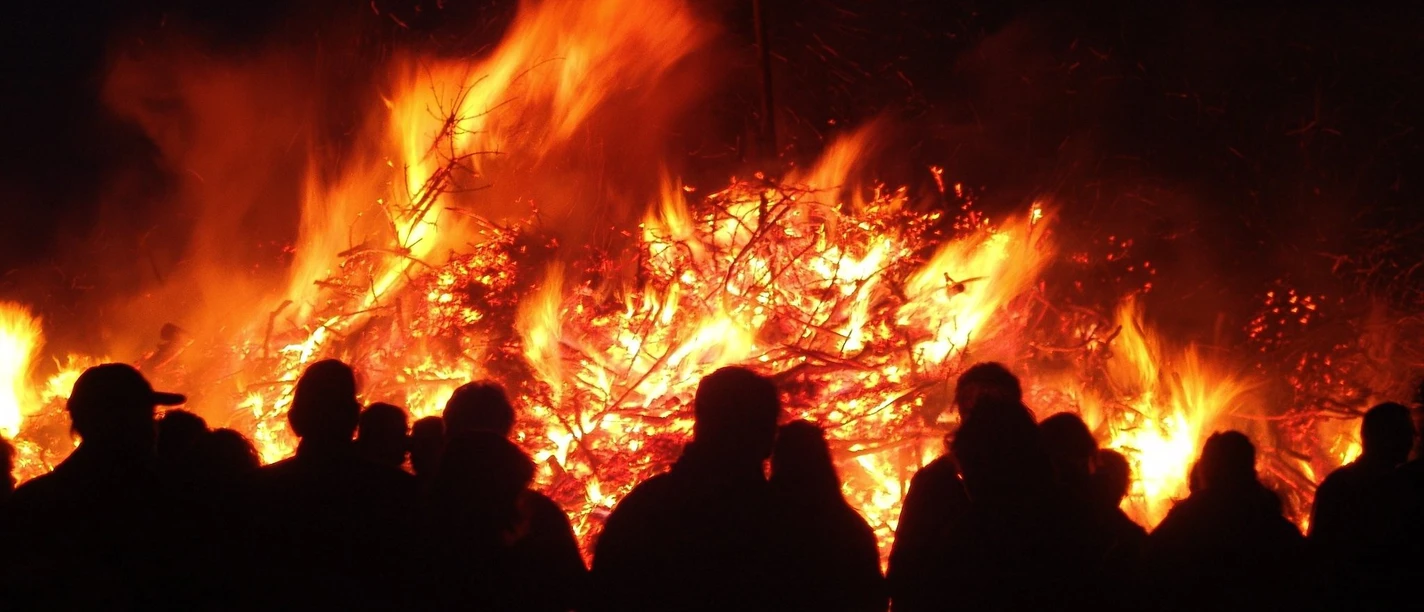 Feuer Personen stehen vor einem großen, lodernden Feuer in der Dunkelheit, die Flammen erhellen die Nacht.