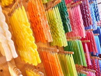 Auswahl an verschiedenen Kerzen Bunte, gedrehte Kerzen in verschiedenen Farben wie Gelb, Orange, Grün und Blau hängen ordentlich an Holzstäben in einem Geschäft.