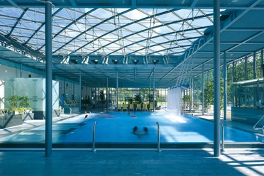 Geibeltbad Pirna: Modern overdekt zwembad met glazen dak, blauw water en meerdere zwemmers; lichte, luchtige sfeer met planten en ligstoelen.