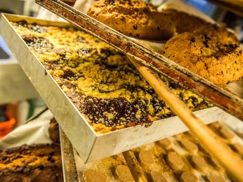 Bio-Bäckerei Schmilka Backblech mit Streuselkuchen und Brotlaiben in einem Backofen, warme, einladende Atmosphäre.