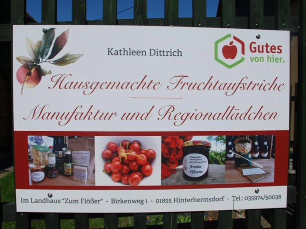 Hausgemachte Fruchtaufstriche Schild mit der Aufschrift "Hausgemachte Fruchtaufstriche, Manufaktur und Regionallädchen" und Bildern von Produkten, Kirschen und einem Marmeladenglas.