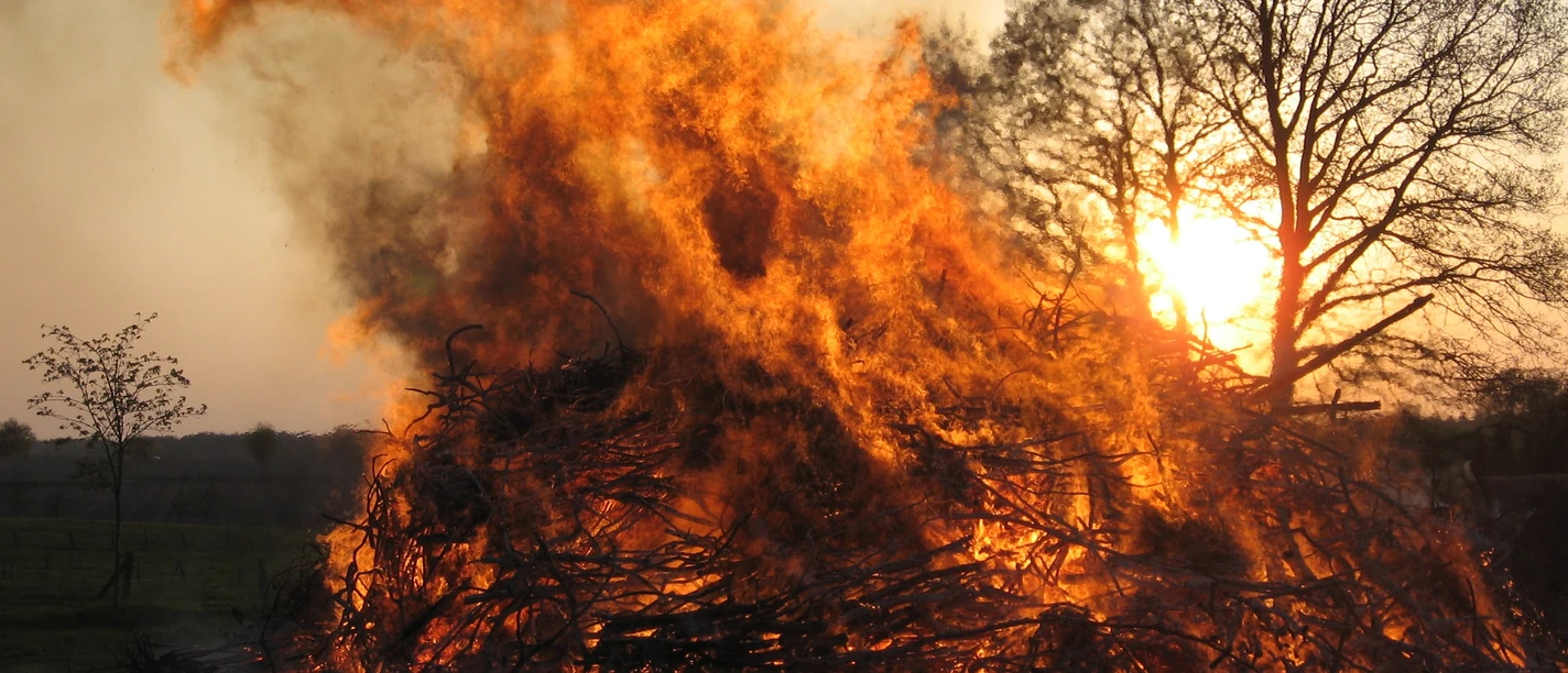Osterfeuer Ein großes, hell loderndes Osterfeuer aus Ästen und Zweigen vor der untergehenden Sonne.