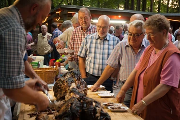 bispingen-spanferkel-4395.jpg Menschen servieren und teilen Spanferkel bei einem traditionellen Dorffest auf dem Grillplatz in Volkwardingen.