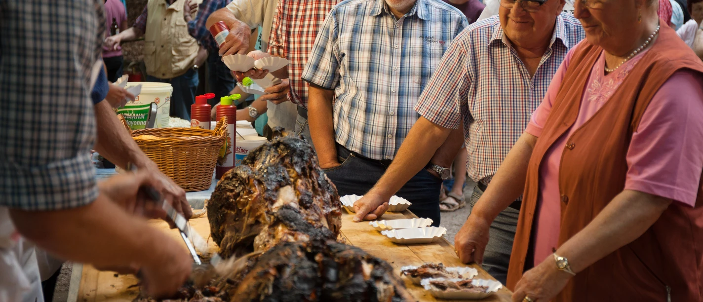 bispingen-spanferkel-4395.jpg Menschen servieren und teilen Spanferkel bei einem traditionellen Dorffest auf dem Grillplatz in Volkwardingen.