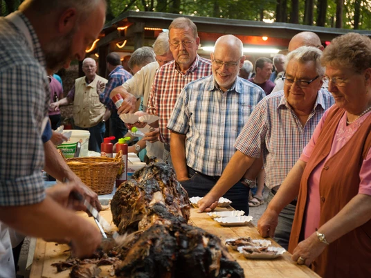 bispingen-spanferkel-4395.jpg Menschen servieren und teilen Spanferkel bei einem traditionellen Dorffest auf dem Grillplatz in Volkwardingen.