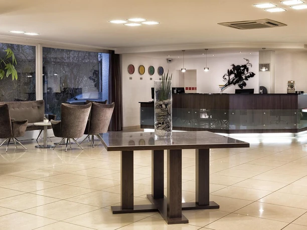 Ein modernes Lobby mit eleganten Stühlen und einem Empfangstresen. Helle Farben und Pflanzen schaffen eine einladende Atmosphäre.