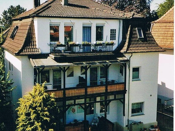 Garten Ein modernes, mehrstöckiges Haus mit einem Balkon und einem schönen Garten. Die Fassade ist hell und freundlich, umgeben von Bäumen und Sträuchern.