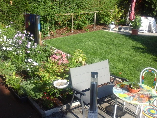 015 (2) Ein schöner Garten mit bunten Blumen und grünem Rasen. Es gibt einen Tisch und Stühle zum Entspannen.