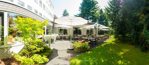 Sonnenterrasse des Hotels Gronauer Tannenhof mit weißen Schirmen, Tischen und Garten