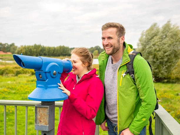 Delbrueck-Steinhorster Becken-Teutoburger-Wald-Tourismus-D-Ketz-059.jpg Paar in bunter Outdoor-Kleidung blickt durch blaues Fernrohr auf Landschaft von einer Aussichtsplattform.