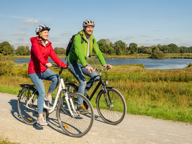 Delbrueck-Steinhorster Becken-Teutoburger-Wald-Tourismus-D-Ketz-074.jpg Zwei Radfahrer genießen eine Fahrt auf einem Schotterweg durch eine idyllische Landschaft mit Fluss.