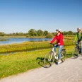 Delbrueck-Steinhorster Becken-Teutoburger-Wald-Tourismus-D-Ketz-098.jpg Zwei Radfahrer auf Schotterweg entlang eines Sees bei Sonnenschein; grüne Landschaft im Hintergrund.