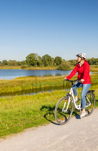 Delbrueck-Steinhorster Becken-Teutoburger-Wald-Tourismus-D-Ketz-098.jpg Zwei Radfahrer auf Schotterweg entlang eines Sees bei Sonnenschein; grüne Landschaft im Hintergrund.