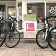IMG_0570.jpg Vier E-Bikes stehen auf einer gepflasterten Fläche vor einem Tourist-Informationszentrum.
