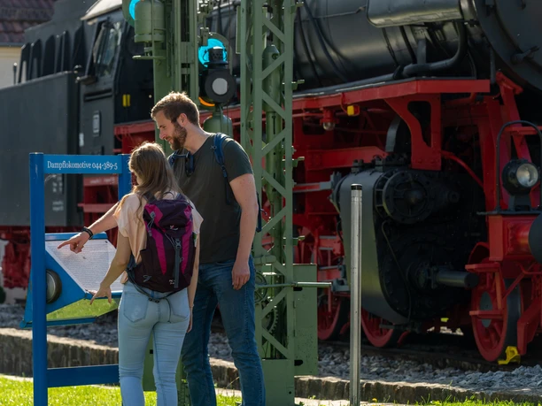 Ein Mann und eine Frau stehen vor der schwarzen Dampflokomotive am Bahnhof Altenbeken