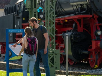 Altenbeken-Lokomotive-044er-Teutoburger-Wald-Tourismus-Patrick-Gawandtka-034.jpg Ein Mann und eine Frau stehen vor der schwarzen Dampflokomotive am Bahnhof Altenbeken