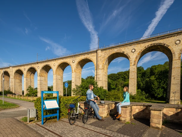 Personen entspannen vor dem beeindruckenden Altenbeken-Viadukt, einem markanten Eisenbahn-Bauwerk.