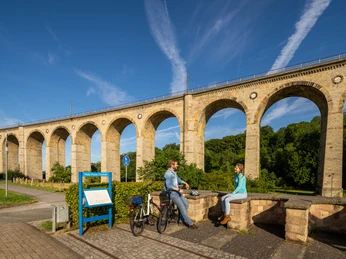 Altenbeken-Viadukt-Teutoburger-Wald-Tourismus-Patrick-Gawandtka-022.jpg Personen entspannen vor dem beeindruckenden Altenbeken-Viadukt, einem markanten Eisenbahn-Bauwerk.