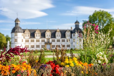 Paderborn-SchlossNeuhaus-Teutoburger-Wald-Tourismus-Patrick-Gawandtka-123.jpg Schloss Neuhaus vor strahlend blauem Himmel, umgeben von einem prächtigen Garten mit bunten Blumen.