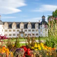 Paderborn-SchlossNeuhaus-Teutoburger-Wald-Tourismus-Patrick-Gawandtka-123.jpg Schloss Neuhaus vor strahlend blauem Himmel, umgeben von einem prächtigen Garten mit bunten Blumen.