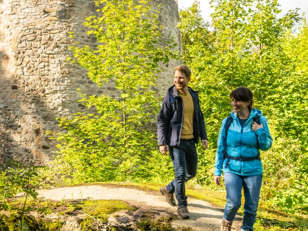 Ein Mann und eine Frau mit Rucksack lächelnd vor der Iburg in Bad Driburg