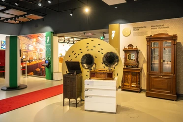 Espelkamp-Schloss Benkhausen-Automatenmuseum-Teutoburger-Wald-Tourismus-D-Ketz-076-CC-BY-SA.jpg Ein Ausstellungsraum mit antiken mechanischen Musikgeräten, darunter Grammophone und Musiktruhen.