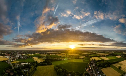Rahden-Teutoburger-Wald-Tourismus-D-Ketz-001.jpg Ein atemberaubender Sonnenuntergang über einer weiten, grünen Landschaft mit vereinzelten Wolken am Himmel.