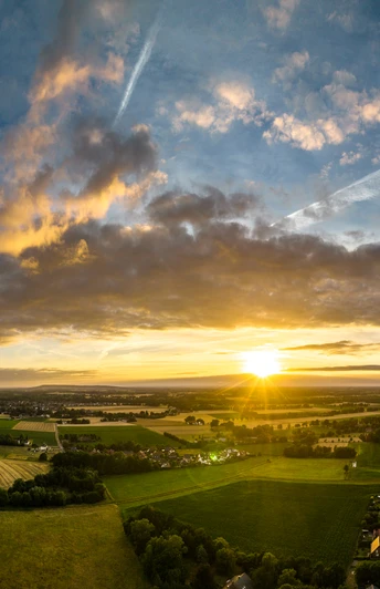 Rahden-Teutoburger-Wald-Tourismus-D-Ketz-001.jpg Ein atemberaubender Sonnenuntergang über einer weiten, grünen Landschaft mit vereinzelten Wolken am Himmel.
