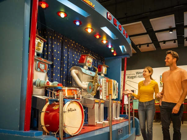 Mann und Frau betrachten eine bunte Roboterband-Ausstellung mit Schlagzeug und Akkordeon in einem Museum.