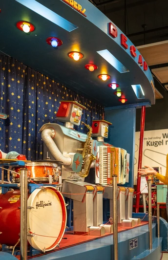 Espelkamp-Schloss Benkhausen-Automatenmuseum-Teutoburger-Wald-Tourismus-D-Ketz-073.jpg Mann und Frau betrachten eine bunte Roboterband-Ausstellung mit Schlagzeug und Akkordeon in einem Museum.