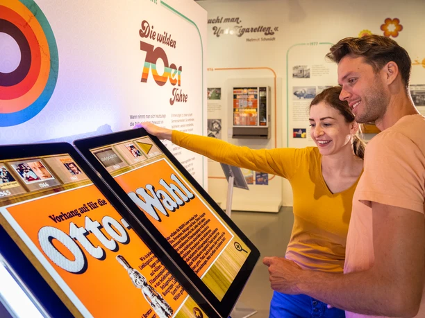 Espelkamp-Schloss Benkhausen-Automatenmuseum-Teutoburger-Wald-Tourismus-D-Ketz-075.jpg Ein Paar betrachtet interaktive Bildschirme in einer Ausstellung über die wilden 70er Jahre.