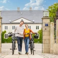 Espelkamp-Schloss Benkhausen-Teutoburger-Wald-Tourismus-D-Ketz-087.jpg Ein junges Paar schiebt lächelnd Fahrräder durch ein steinernes Tor vor einem historischen Gebäude.