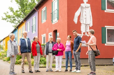 Gruppe von Menschen steht vor buntem Gebäude mit großer, weißer Figur in Espelkamp.