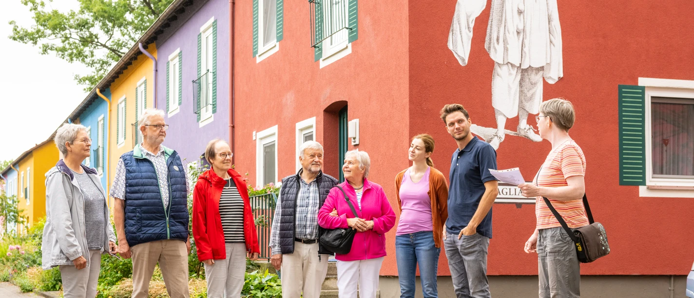 Espelkamp-Stadtführung-Teutoburger-Wald-Tourismus-D-Ketz-117.jpg Gruppe von Menschen steht vor buntem Gebäude mit großer, weißer Figur in Espelkamp.