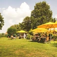 Schirmbar (Jens Butz).jpg Blick auf eine Wiese mit mehreren Sitzplätzen, gelben Sonnenschirmen und Menschen, die dort zusammensitzen und sich unterhalten