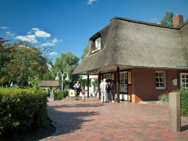 Blick auf Pelz vom Lüneburger Damm.jpg Blick auf eine Eisdiele in einem Reetdachhaus, vor der Menschen stehen und in einer Schlange auf ihr Eis warten